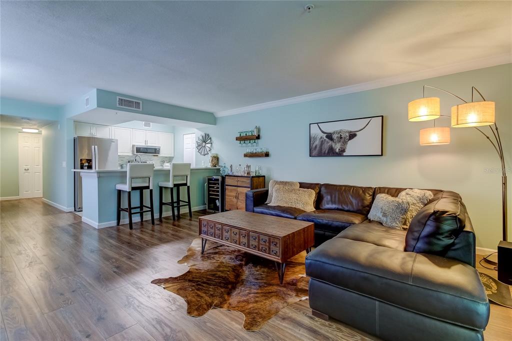 A hallway with wood-look flooring connects a white entry door to a kitchen with stainless appliances — 2400 FEATHER SOUND DRIVE UNIT 1228, CLEARWATER, FL