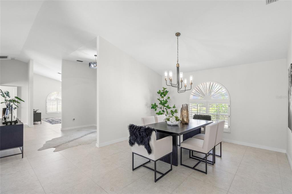A bright dining room features a dark table, modern chandelier, and arched windows with shutters — 1527 BUOY LANE, OSPREY, FL