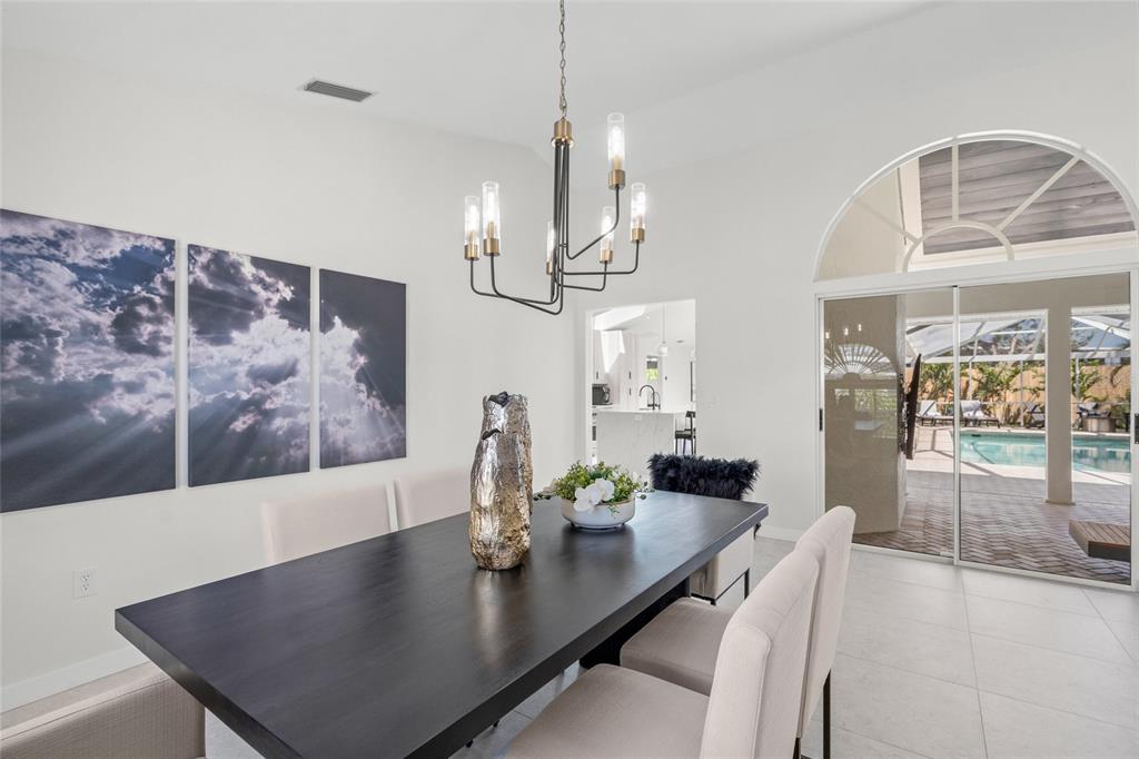 A dining room features a dark wood table, a modern chandelier, and sliding glass doors — 1527 BUOY LANE, OSPREY, FL