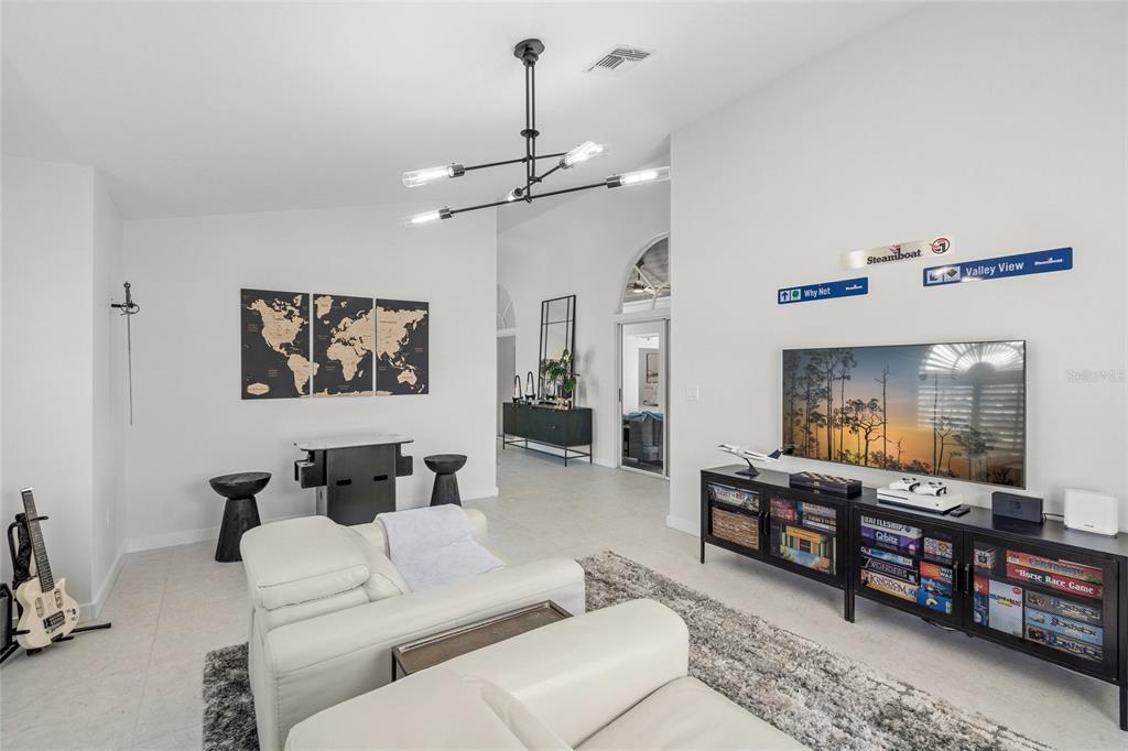 A living room features white walls, a modern chandelier, a television, and a board game console — 1527 BUOY LANE, OSPREY, FL