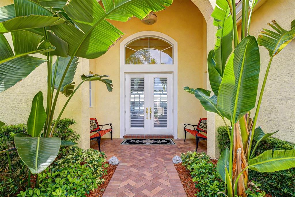 A brick walkway leads to a double front door flanked by benches and large tropical plants — 5056 RUBY FLATS DRIVE, WIMAUMA, FL