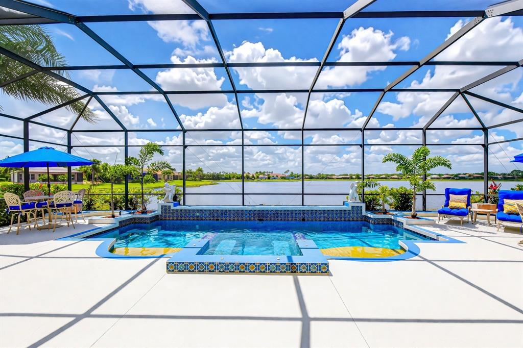 A screened-in swimming pool and spa overlook a lake under a bright blue sky — 5056 RUBY FLATS DRIVE, WIMAUMA, FL