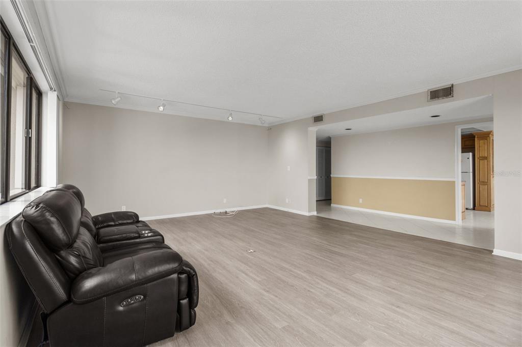 A living room with light wood-look flooring, a dark leather sofa, and track lighting — 150 BELLEVIEW BOULEVARD UNIT 507, BELLEAIR, FL