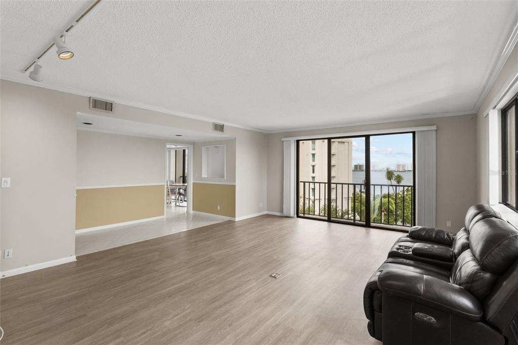 A living room with wood-look flooring, a black leather sofa, and a balcony overlooking water — 150 BELLEVIEW BOULEVARD UNIT 507, BELLEAIR, FL