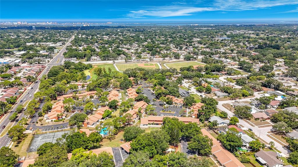 An aerial view shows a residential complex with multiple buildings, parking areas, and nearby sports fields — 1935 PEPPERMILL DRIVE UNIT C, CLEARWATER, FL