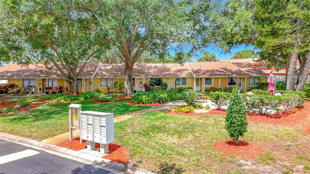 A row of single-story yellow townhomes with a central mailbox station and mature trees — 1935 PEPPERMILL DRIVE UNIT C, CLEARWATER, FL