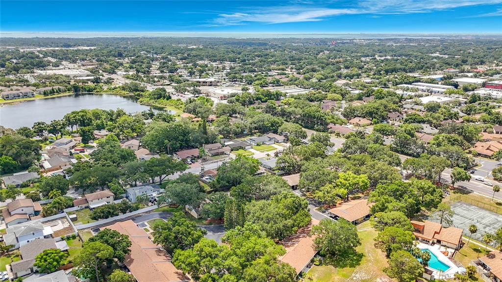 An aerial view shows a suburban neighborhood with houses, trees, a lake, and a pool — 1935 PEPPERMILL DRIVE UNIT C, CLEARWATER, FL