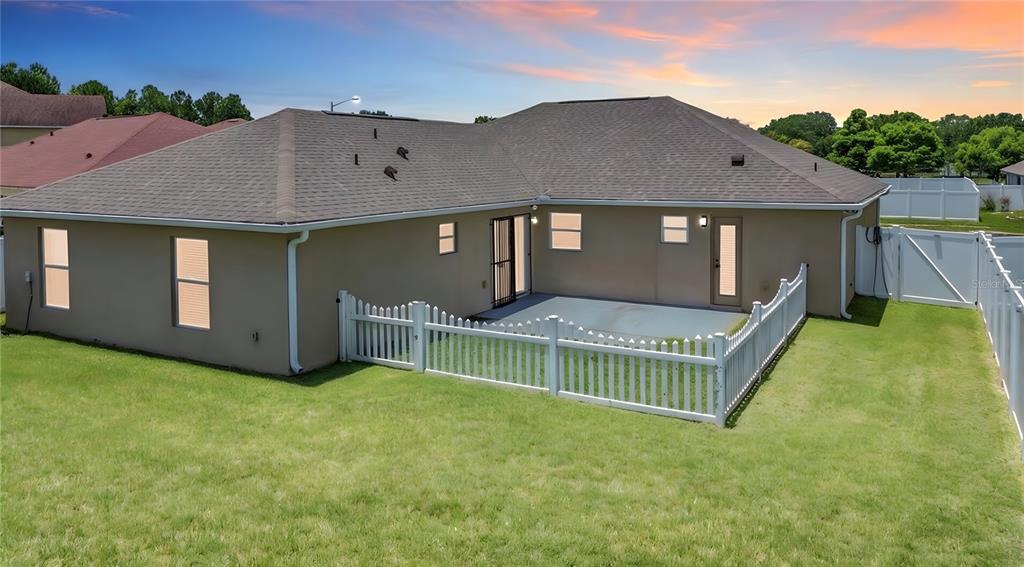The exterior rear view of a house features a concrete patio and a white fence — 3013 MANDOLIN DRIVE, KISSIMMEE, FL