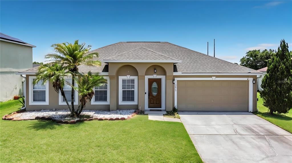 A single-story house with a tan stucco exterior, a two-car garage, and a palm tree — 3013 MANDOLIN DRIVE, KISSIMMEE, FL