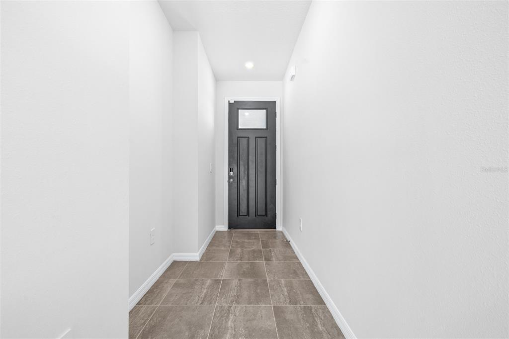 A narrow entryway features white walls, a dark front door, and gray tiled flooring — 2707 VIRGINIA PINE DRIVE, BARTOW, FL