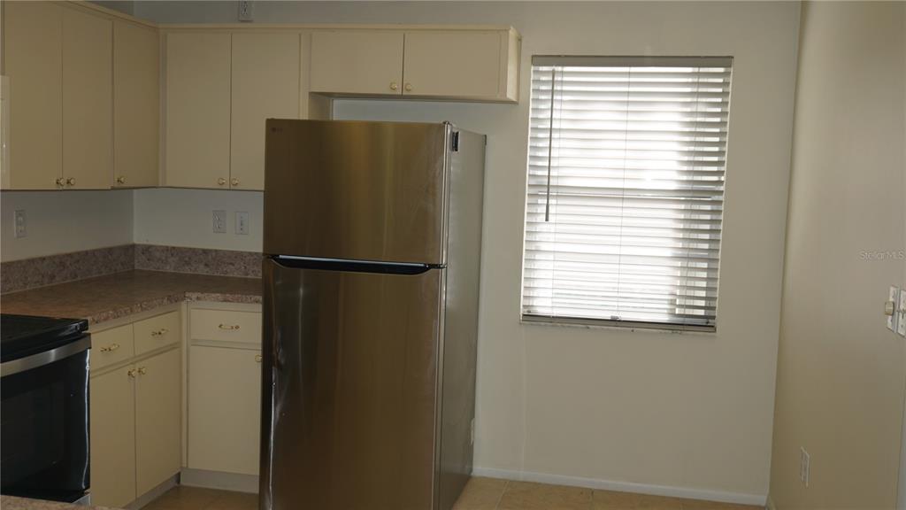 A kitchen features light-colored cabinets, a stainless steel refrigerator, and a window with blinds — 8907 SEELEY LANE, HUDSON, FL