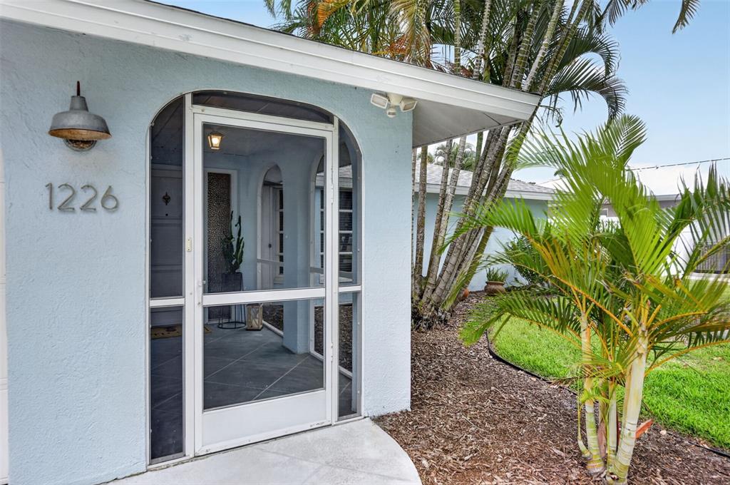 A light blue house exterior features a screened-in entryway with a concrete walkway — 1226 PINE NEEDLE ROAD, VENICE, FL