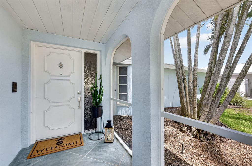A white front door with a pineapple doormat sits inside a screened-in entryway — 1226 PINE NEEDLE ROAD, VENICE, FL