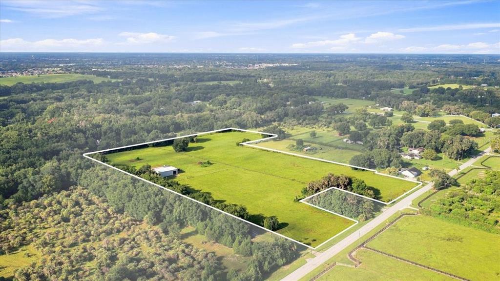 A dirt road runs alongside a large, fenced grassy field with a metal building beyond — SE SUNSET HARBOR ROAD, WEIRSDALE, FL