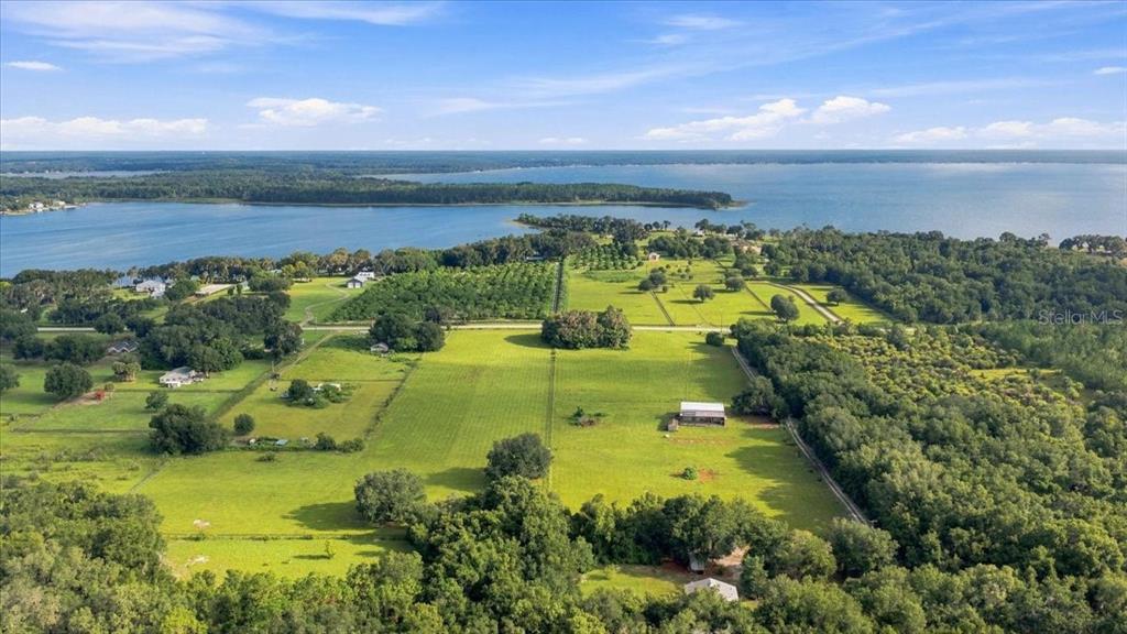 A large, grassy, fenced pasture is surrounded by trees under a blue sky — SE SUNSET HARBOR ROAD, WEIRSDALE, FL