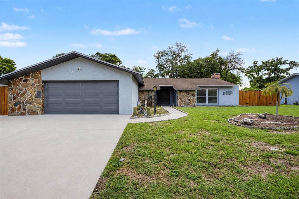 A single-story house with a stone facade, a gray garage door, and a concrete driveway — 3110 SHADOW OAKS DRIVE, HOLIDAY, FL