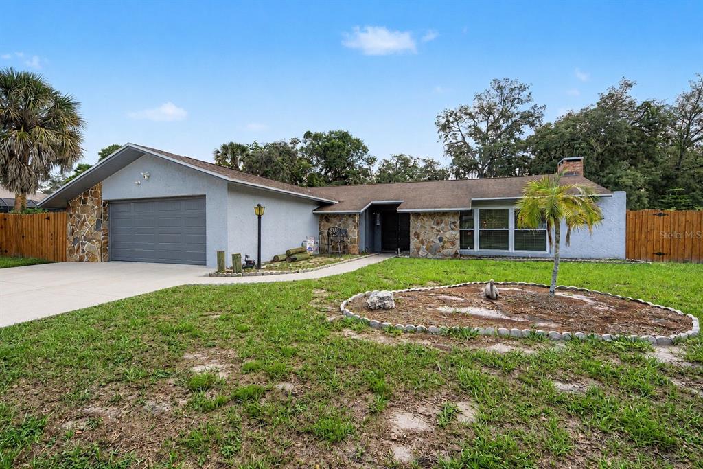 A single-story house with a stone facade, a gray garage door, and a front lawn — 3110 SHADOW OAKS DRIVE, HOLIDAY, FL