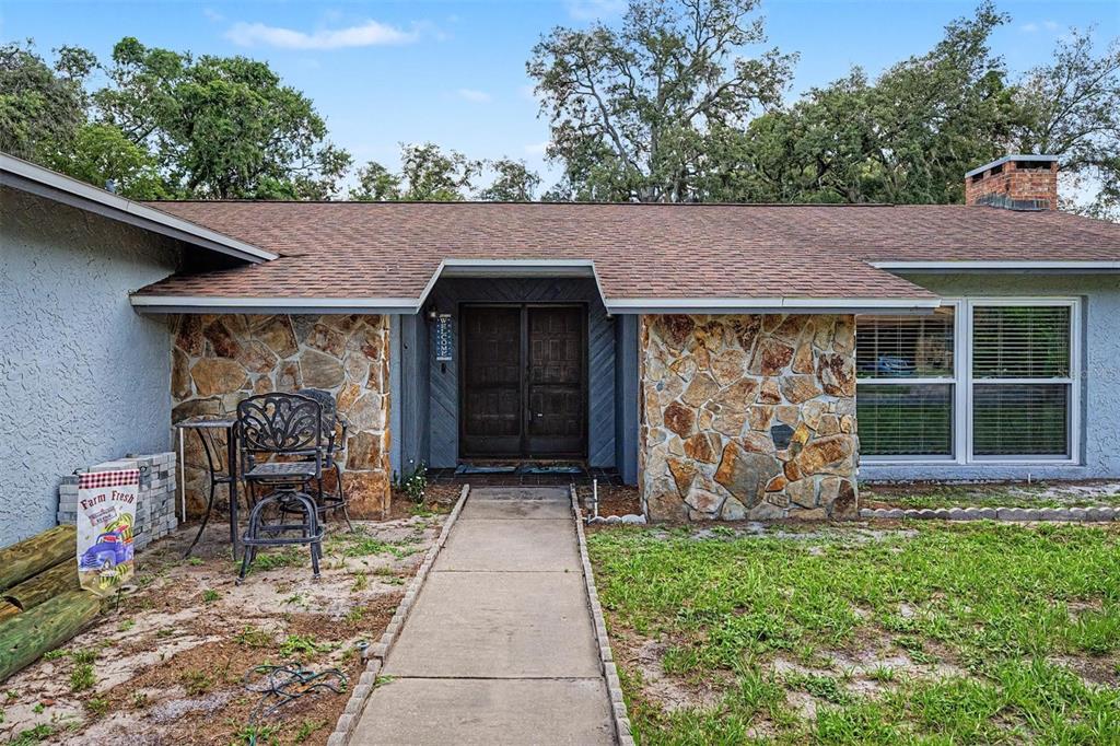 A single-story house exterior features a stone facade, double front doors, and a concrete walkway — 3110 SHADOW OAKS DRIVE, HOLIDAY, FL
