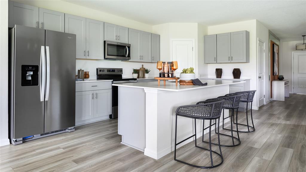 A modern kitchen features light gray cabinets, stainless steel appliances, a white island, and barstools — 36683 THORNHEDGE DRIVE, ZEPHYRHILLS, FL