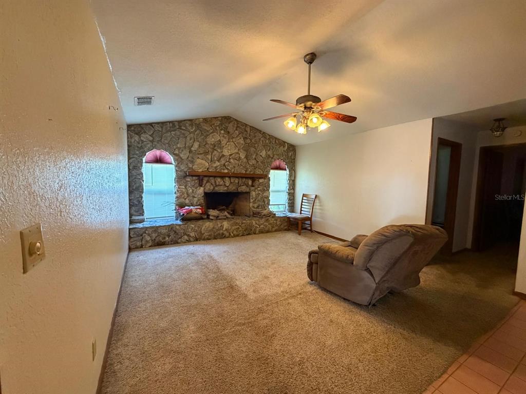 A living room features a stone fireplace, beige carpeting, and a ceiling fan — 215 SANTA ROSA DRIVE, WINTER HAVEN, FL