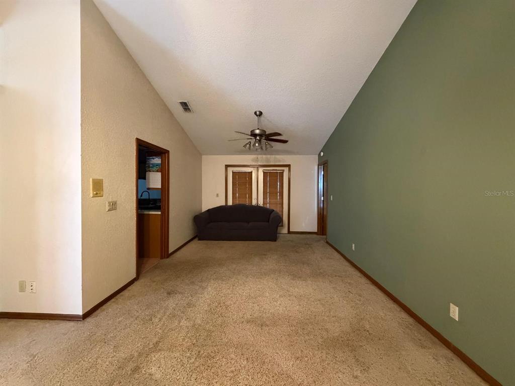 A living room with beige carpet, a vaulted ceiling, and one green accent wall — 215 SANTA ROSA DRIVE, WINTER HAVEN, FL