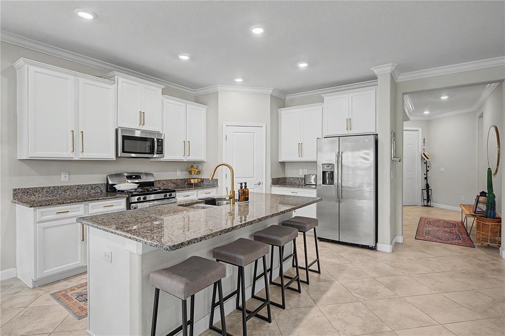 A kitchen features white cabinets, granite countertops, a central island with bar stools, and stainless appliances — 4447 TUBULAR RUN, LAND O LAKES, FL