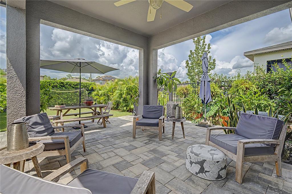 A covered outdoor patio features stone pavers, comfortable seating, and a dining table with umbrella — 4447 TUBULAR RUN, LAND O LAKES, FL
