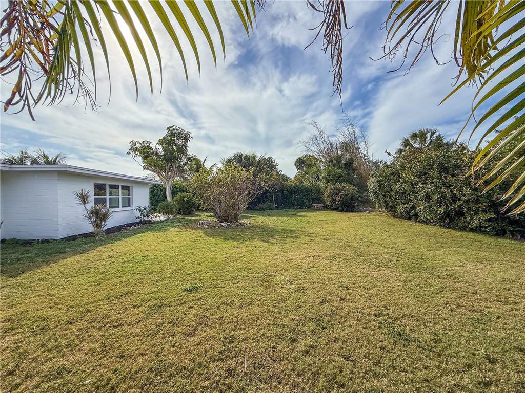 A grassy backyard features a white house exterior, palm fronds, and dense perimeter landscaping — 510 69TH STREET, HOLMES BEACH, FL