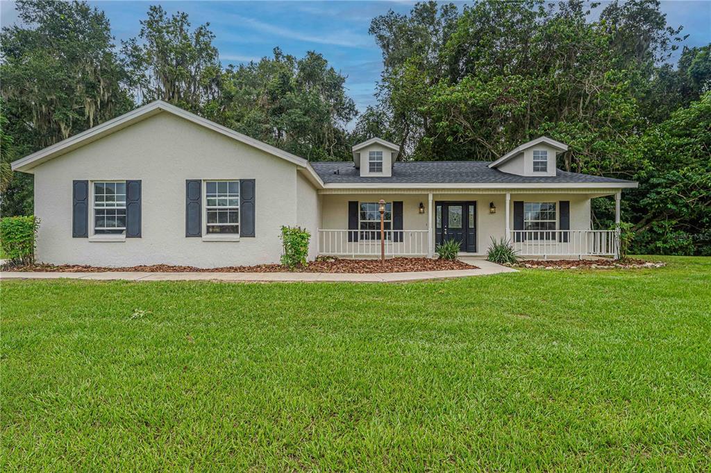 A single-story house with a white stucco exterior, dark shutters, and a front porch — 12615 NW GAINESVILLE ROAD, REDDICK, FL