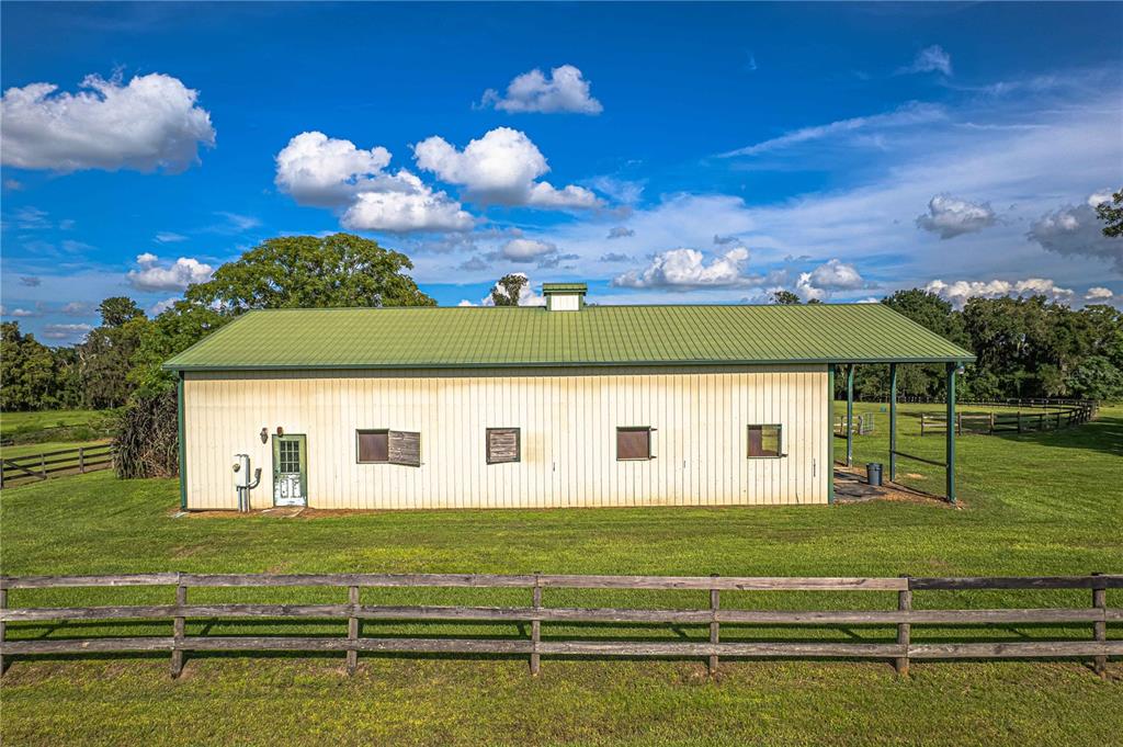 A light-colored barn with a green metal roof sits in a grassy, fenced field — 12615 NW GAINESVILLE ROAD, REDDICK, FL