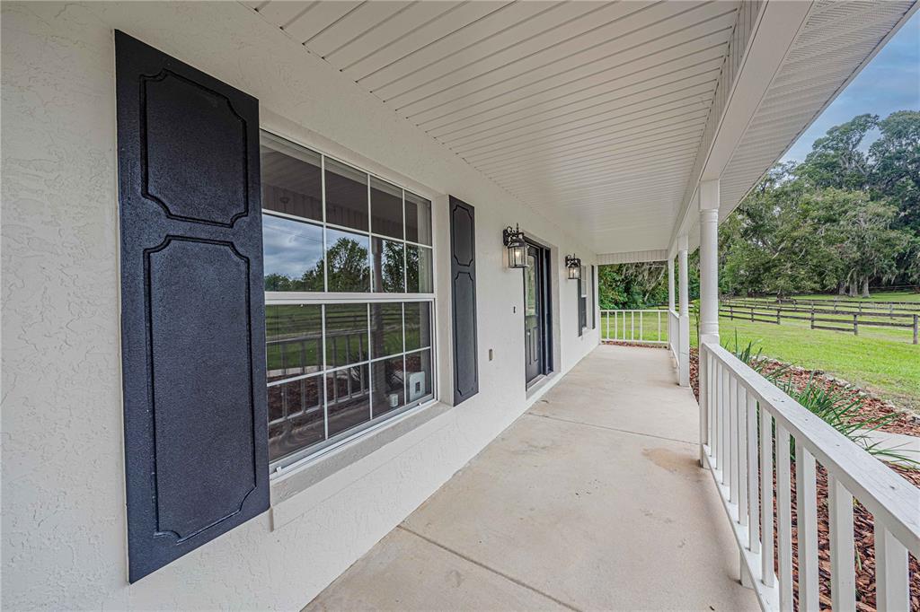 A covered concrete porch features white railings, dark shutters, and a view of a fenced pasture — 12615 NW GAINESVILLE ROAD, REDDICK, FL