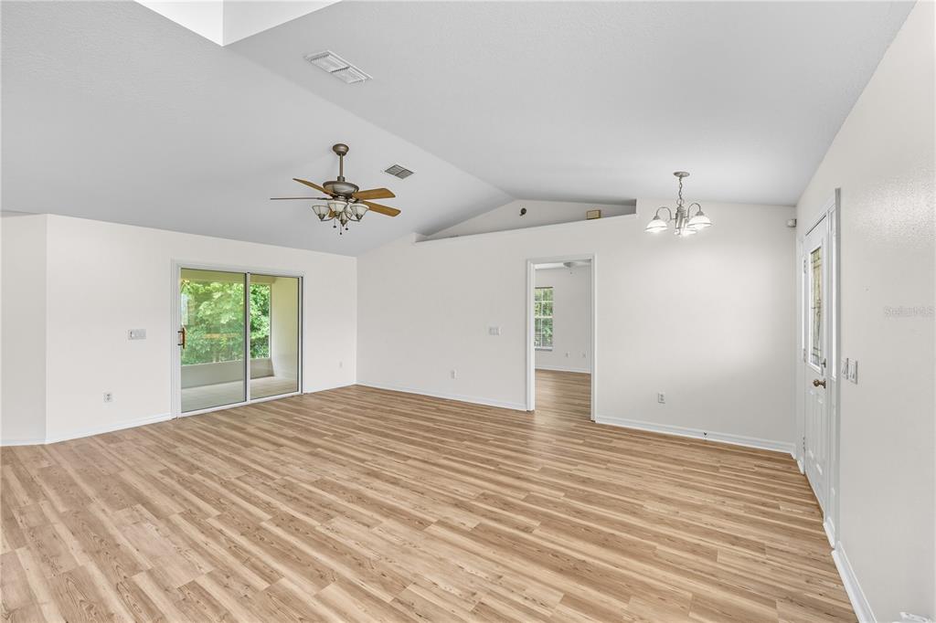 An empty living room features light wood-look flooring, white walls, a vaulted ceiling, and sliding doors — 12615 NW GAINESVILLE ROAD, REDDICK, FL