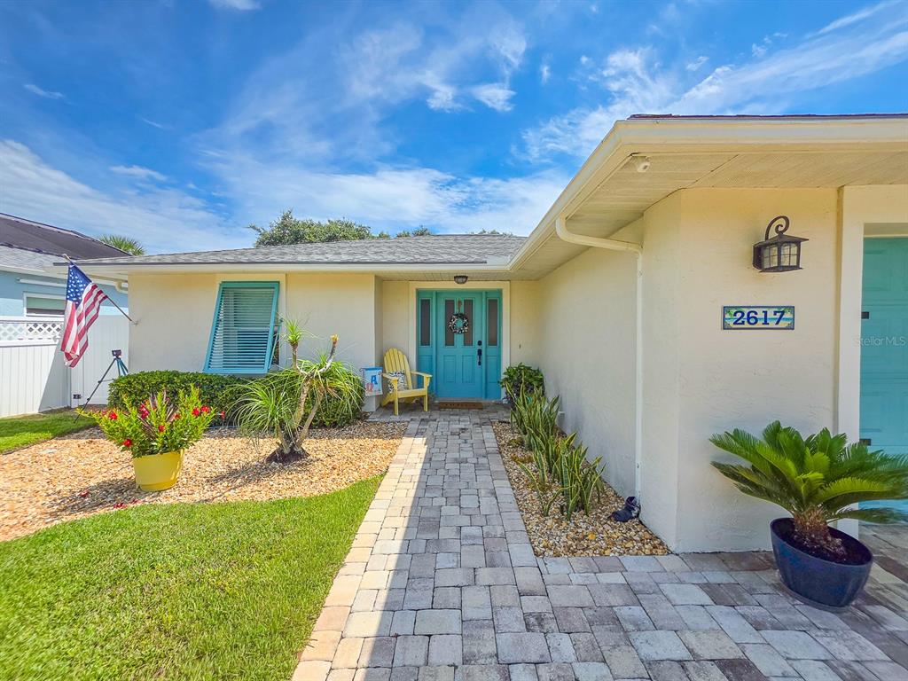 A light-colored house exterior features a turquoise front door, a paver walkway, and landscaping — 2617 S DAYTONA AVENUE, FLAGLER BEACH, FL