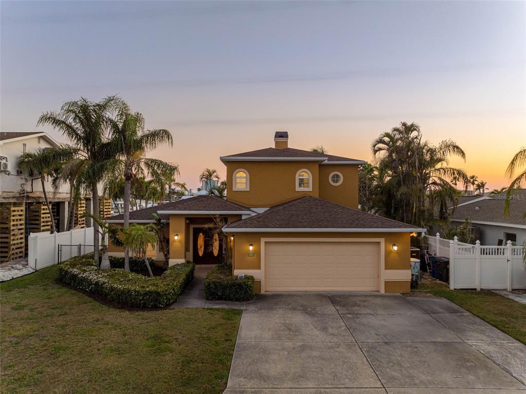 A two-story yellow house with a two-car garage and palm trees at sunset — 11260 5TH STREET E, TREASURE ISLAND, FL