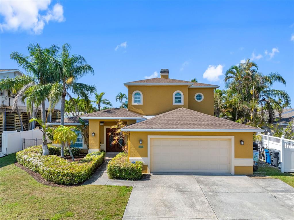 A two-story yellow house with a two-car garage and palm trees in the front yard — 11260 5TH STREET E, TREASURE ISLAND, FL