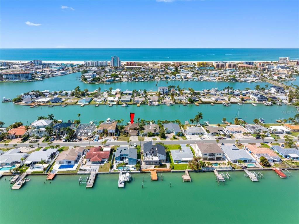 An aerial view shows a waterfront residential neighborhood with docks and a beach in the distance — 11260 5TH STREET E, TREASURE ISLAND, FL