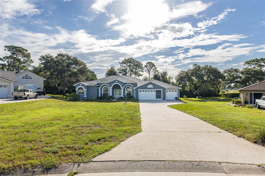 A gray single-story house with a three-car garage and a long concrete driveway — 11382 DOXSEY HILL CIRCLE, SPRING HILL, FL