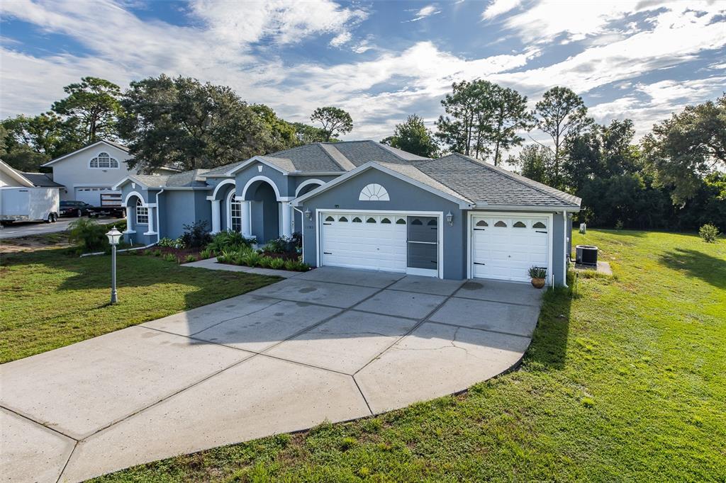 A gray single-story house with a three-car garage and a concrete driveway on a lawn — 11382 DOXSEY HILL CIRCLE, SPRING HILL, FL