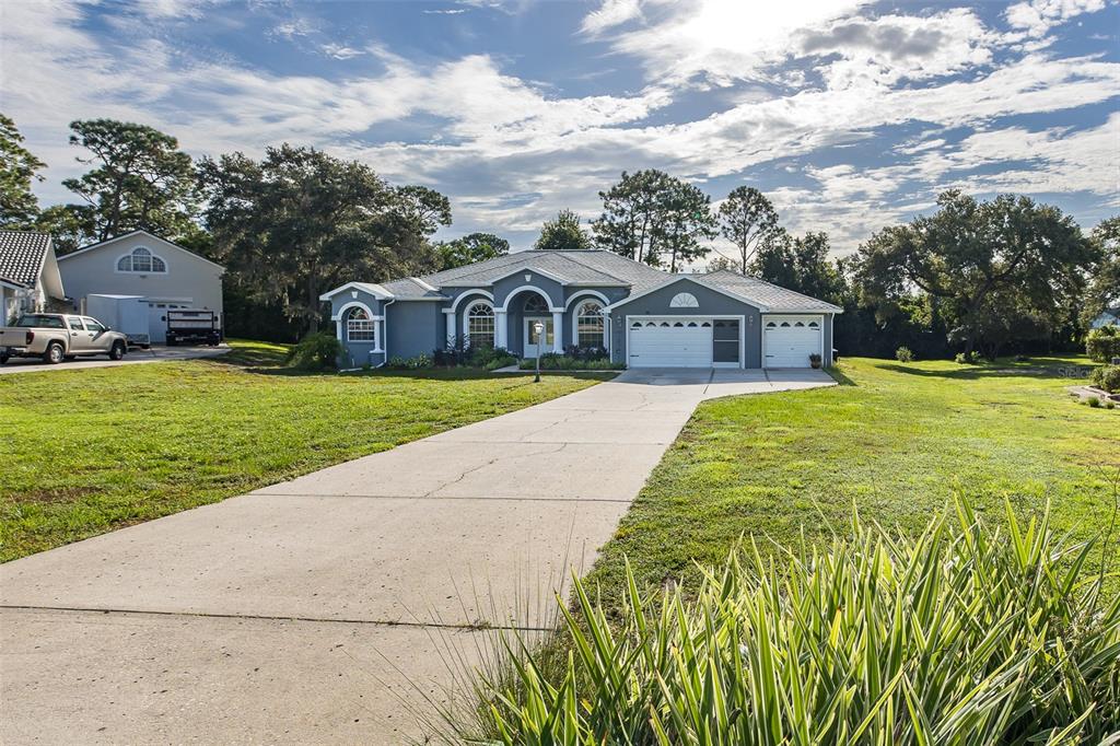 A gray single-story house with a three-car garage and a concrete driveway on a lawn — 11382 DOXSEY HILL CIRCLE, SPRING HILL, FL