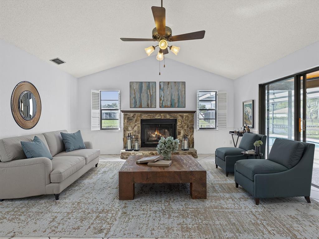 A living room features a stone fireplace, vaulted ceiling, ceiling fan, and blue furniture — 10843 HARBORSIDE DRIVE, LARGO, FL