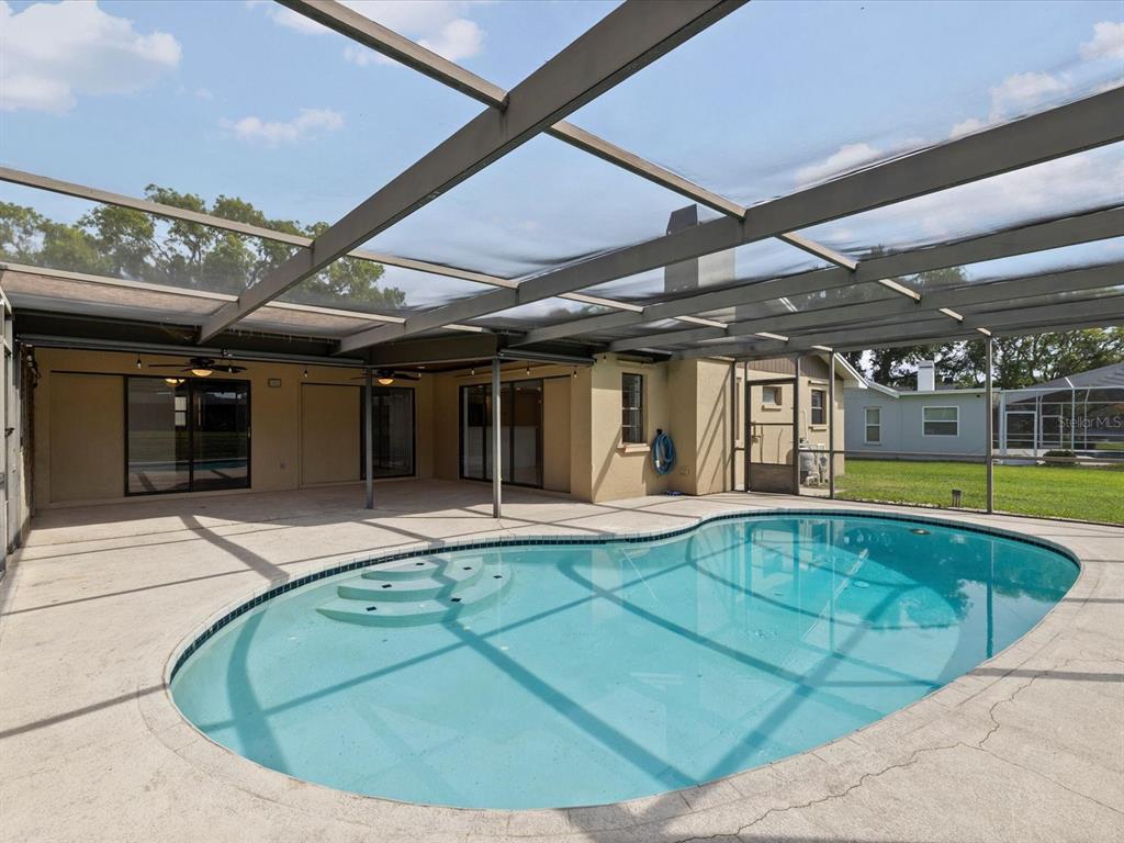 A screened-in patio features a kidney-shaped swimming pool with built-in steps and concrete decking — 10843 HARBORSIDE DRIVE, LARGO, FL