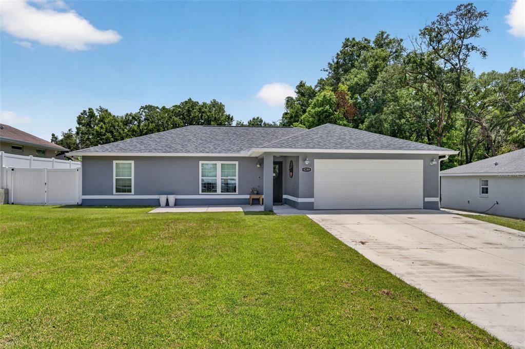 A single-story gray house with a white garage door and a large front lawn — 8280 SE 161ST PLACE, SUMMERFIELD, FL