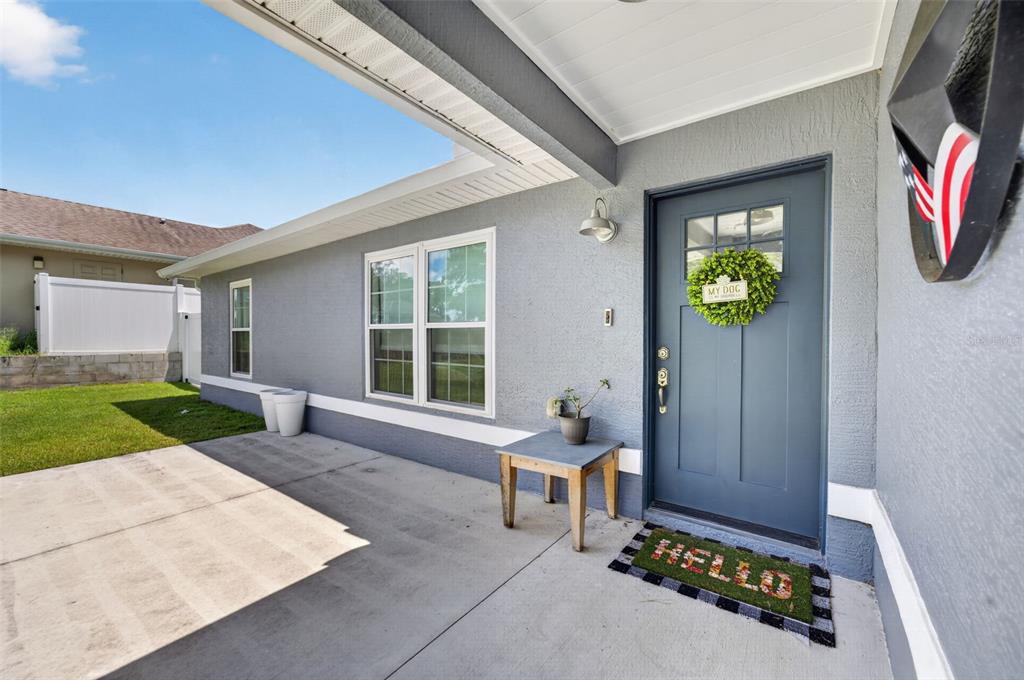 A gray house exterior features a blue front door, a concrete porch, and a wreath — 8280 SE 161ST PLACE, SUMMERFIELD, FL