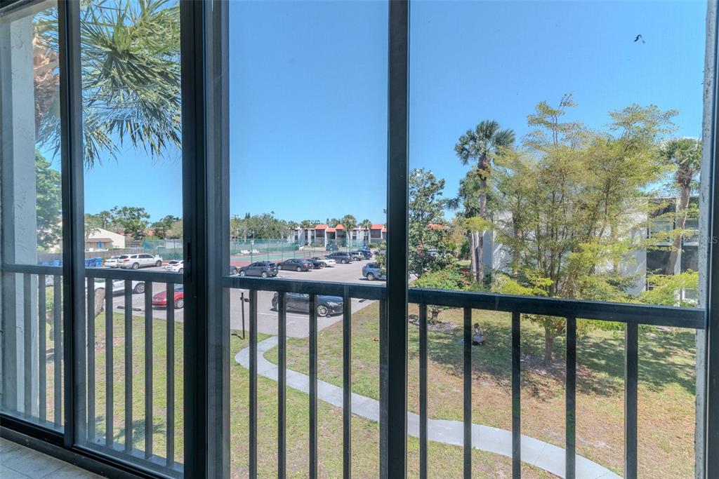 A view from a screened balcony overlooking a parking lot, tennis court, and surrounding trees — 3281 BENEVA ROAD UNIT 202, SARASOTA, FL