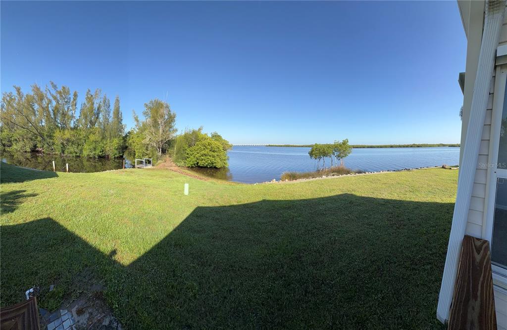 A grassy backyard overlooks a calm body of water with trees along the shoreline — 4300 RIVERSIDE DRIVE UNIT 109, PUNTA GORDA, FL