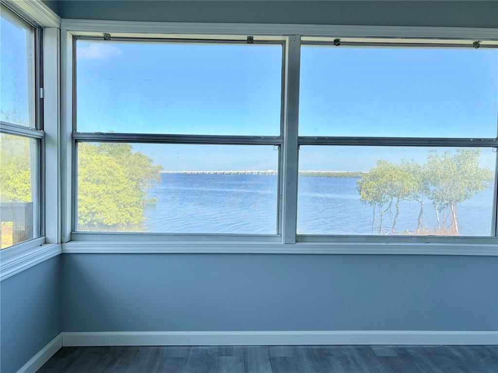 A sunroom with blue walls and gray flooring overlooks a body of water and bridge — 4300 RIVERSIDE DRIVE UNIT 109, PUNTA GORDA, FL
