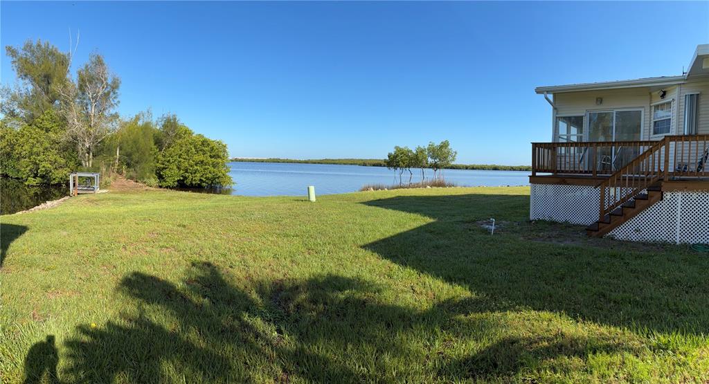A grassy backyard leads to a waterfront view next to a house with a deck — 4300 RIVERSIDE DRIVE UNIT 109, PUNTA GORDA, FL