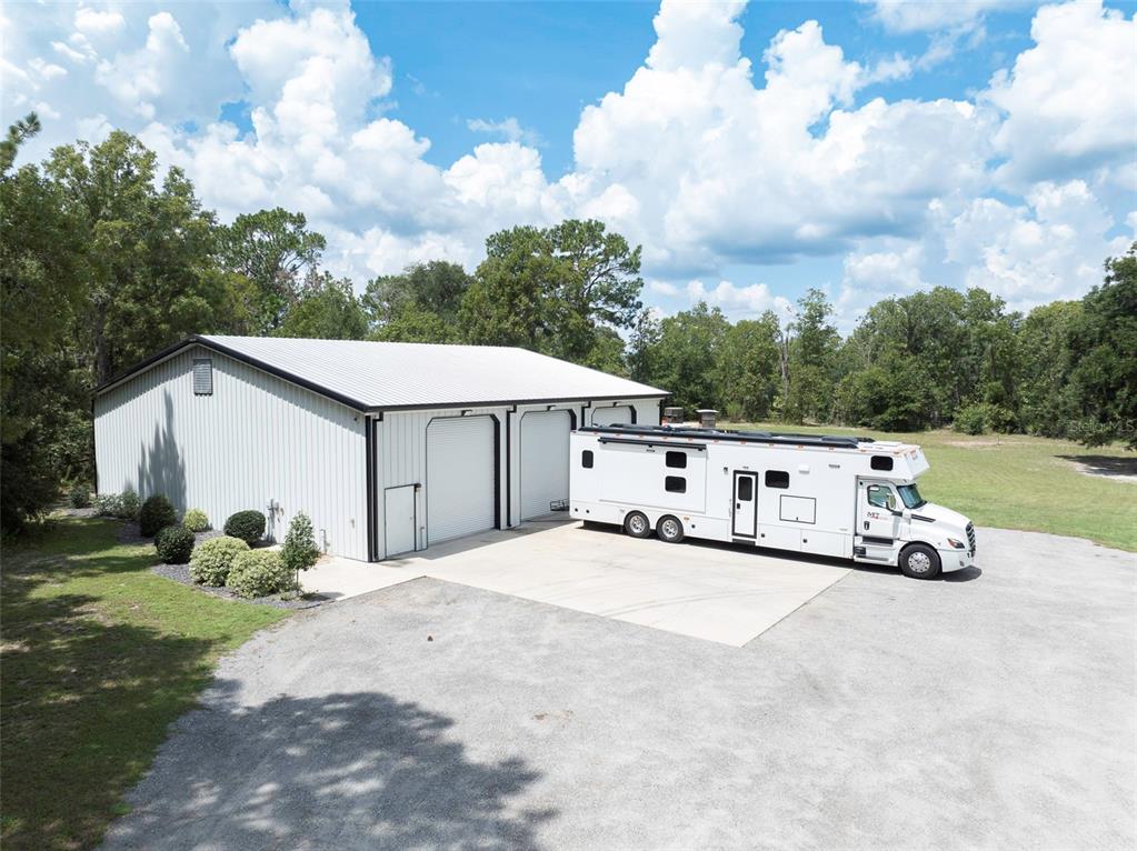 A large metal workshop building sits on a gravel lot next to a parked RV — 2870 NW 87TH AVENUE, WILDWOOD, FL