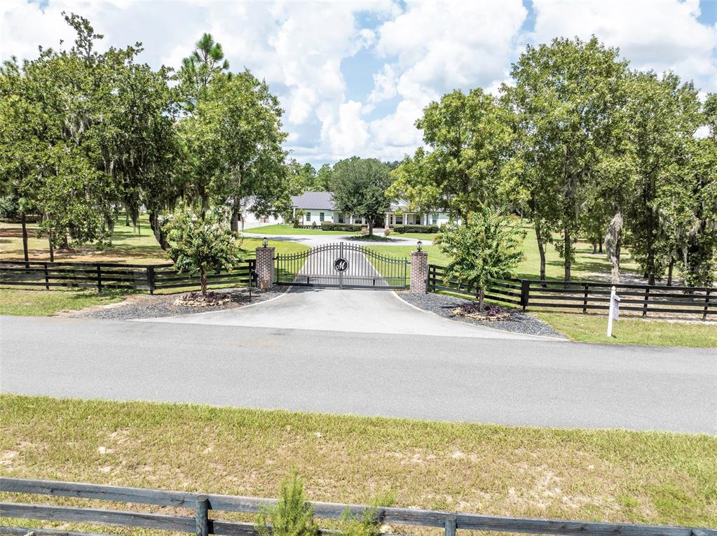 A gated driveway leads to a house surrounded by trees and a wooden fence — 2870 NW 87TH AVENUE, WILDWOOD, FL