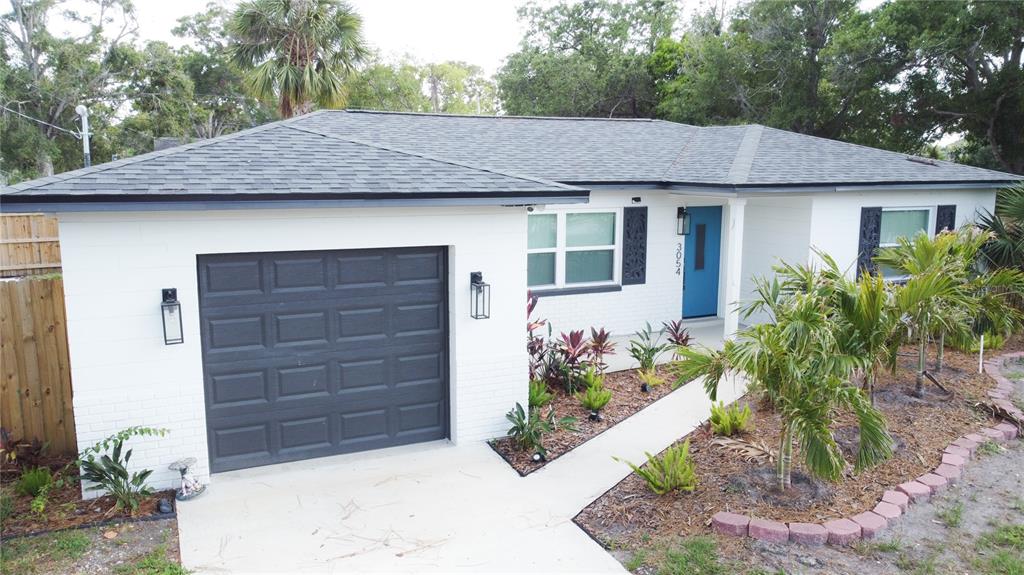 A white brick house with a dark garage door, blue front door, and landscaped front yard — 3054 ADRIAN AVENUE, LARGO, FL
